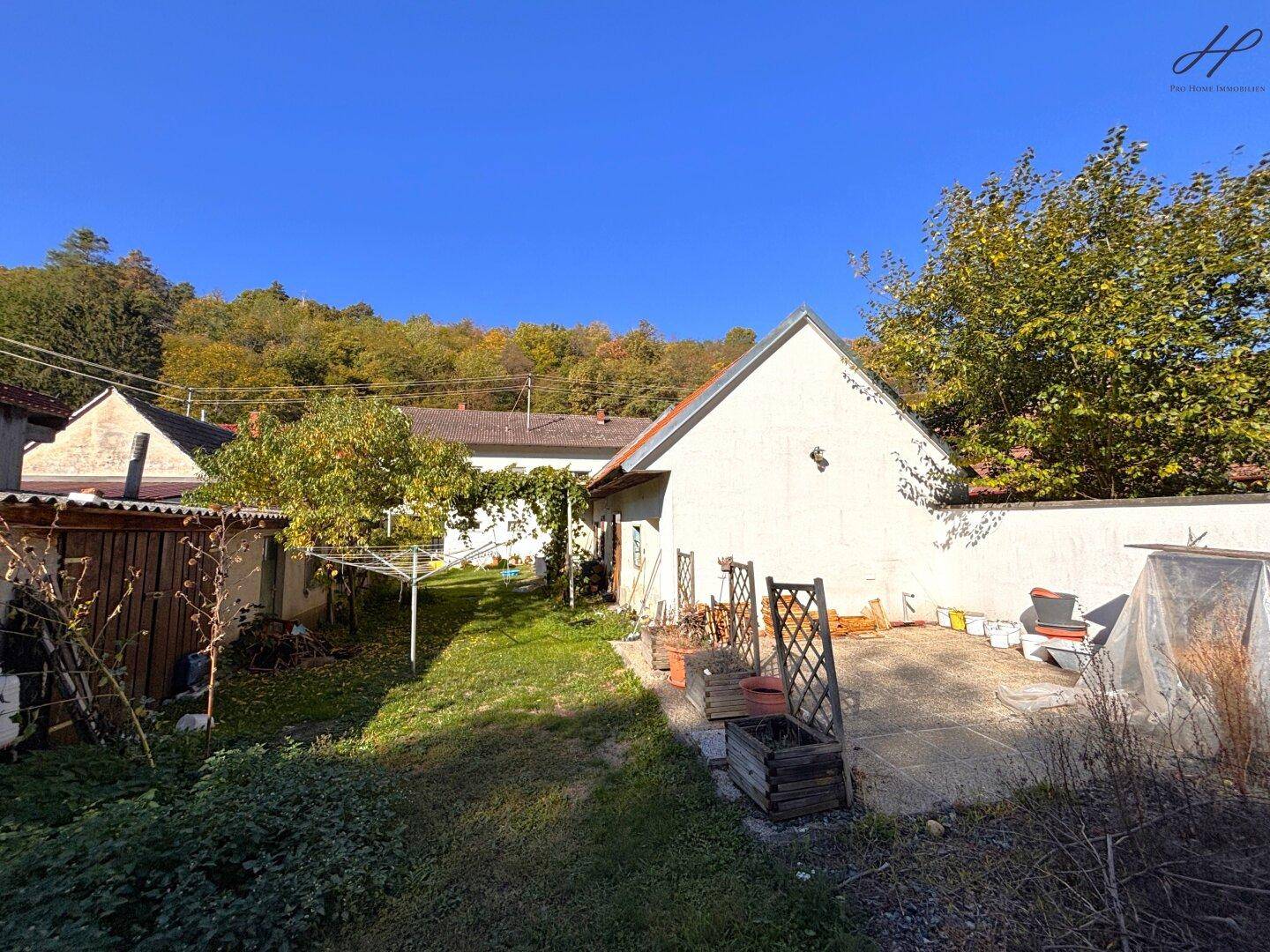 Gartenbereich mit Rasen, Bäumen und einer kleinen Terrasse hinter dem Haus.