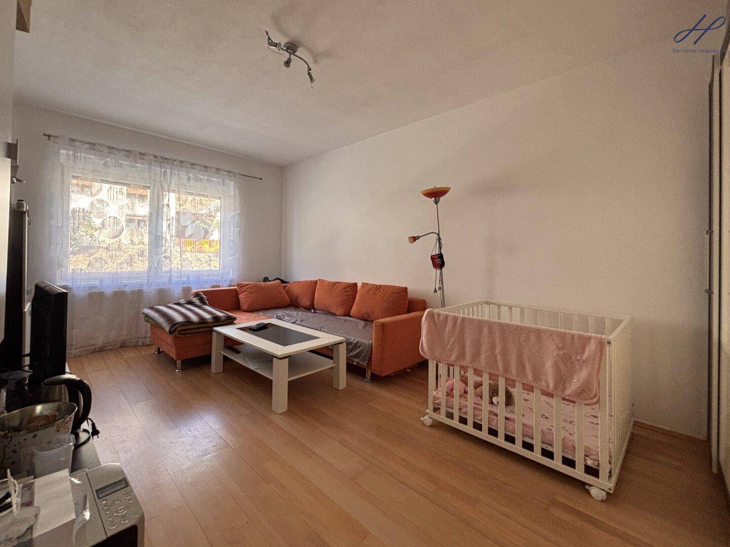 Helles Wohnzimmer mit Ecksofa, Couchtisch und Kinderbett.