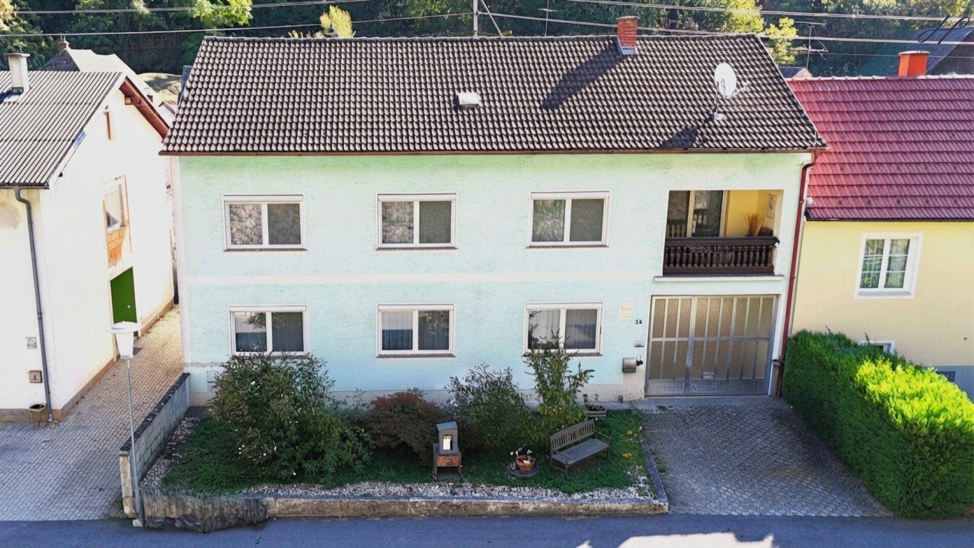 Hausfassade in Hellgrün mit Satteldach, Balkon und Vorgarten.