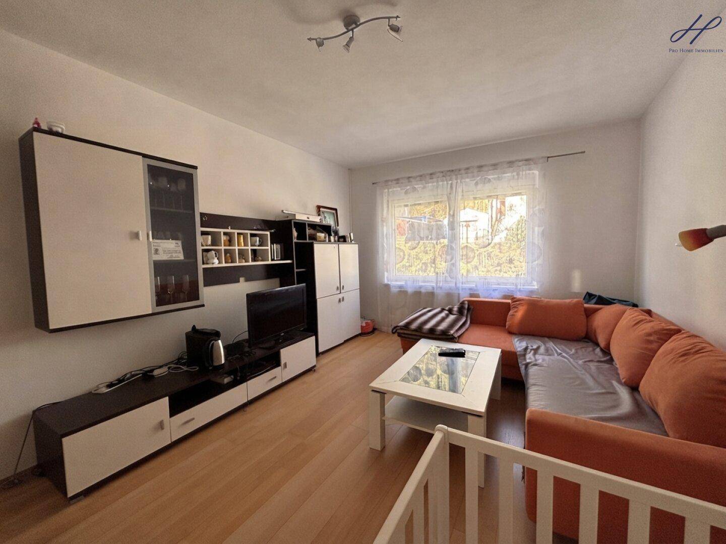 Wohnzimmer mit orangefarbenem Ecksofa, TV-Möbeln und Parkettboden.
