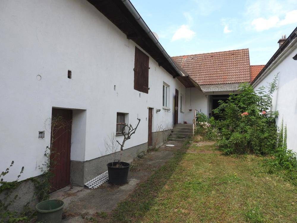 Seitenansicht eines weißen Gebäudes mit Holztüren und einem ungepflegten Gartenbereich daneben.