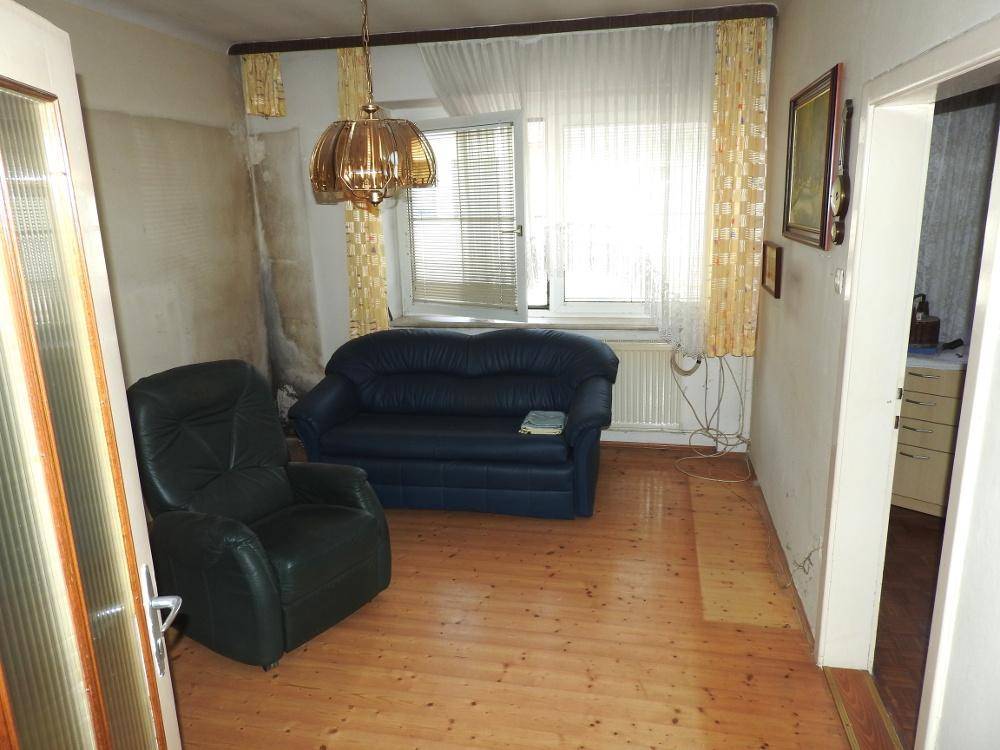 Helles Wohnzimmer mit Holzfußboden, einem blauen Sofa und einem grünen Sessel, bereit zur Renovierung.