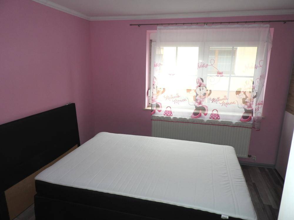Kinderzimmer mit rosa Wänden, Bett und Fenster mit farbenfrohen Vorhängen.