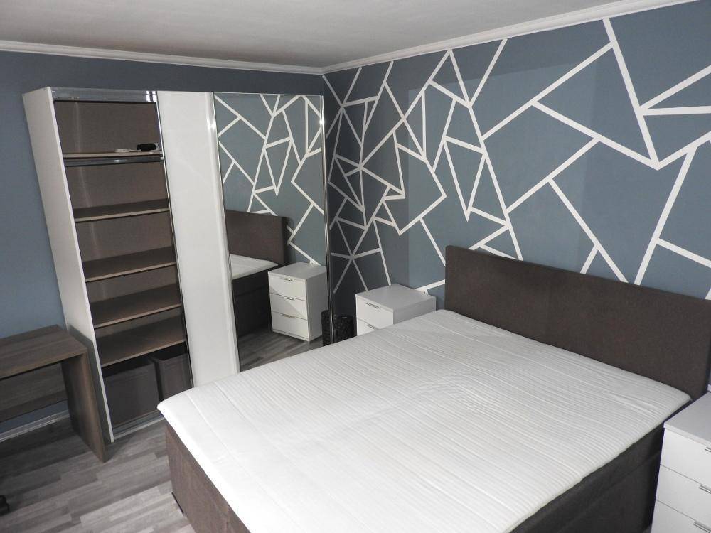 Schlafzimmer mit modernem Kleiderschrank, Doppelbett und geometrischer Wand.