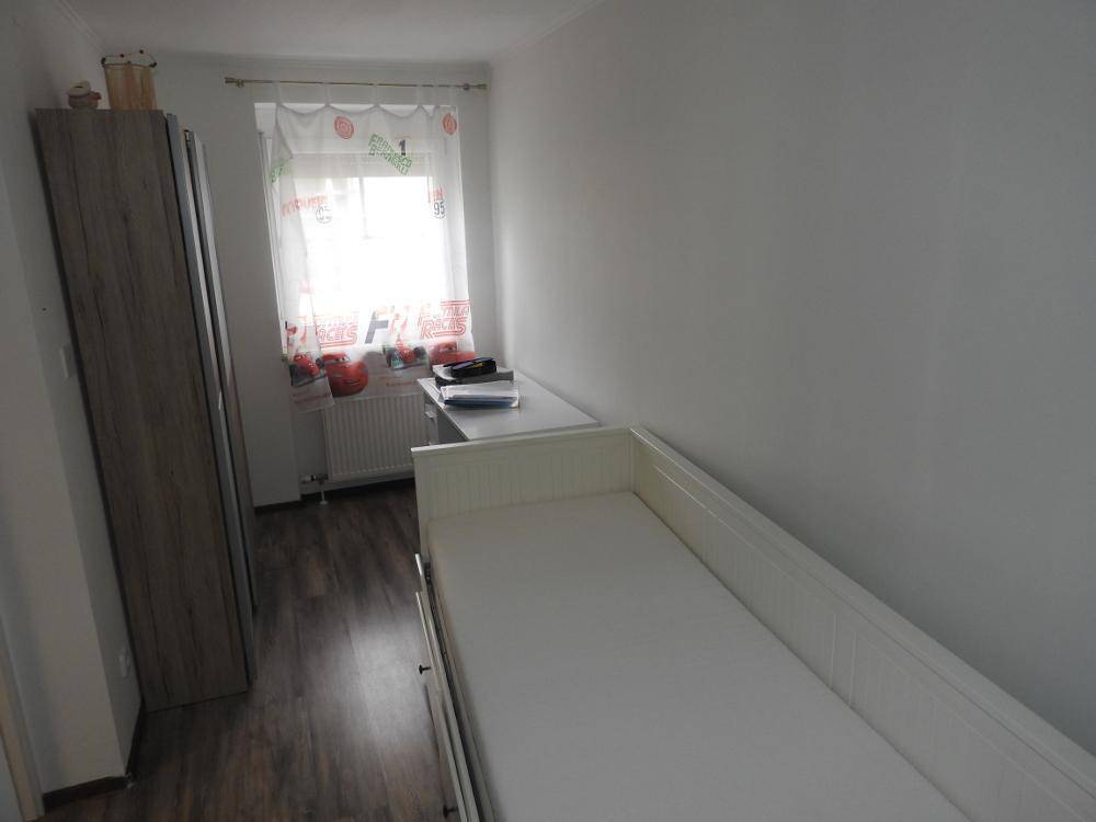 Kinderzimmer mit Einzelbett, Schrank und Fenster mit Vorhängen.