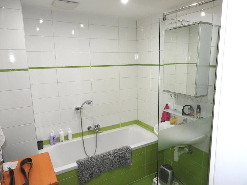 Badezimmer mit Badewanne, Duschabtrennung und grünen Akzentfliesen.