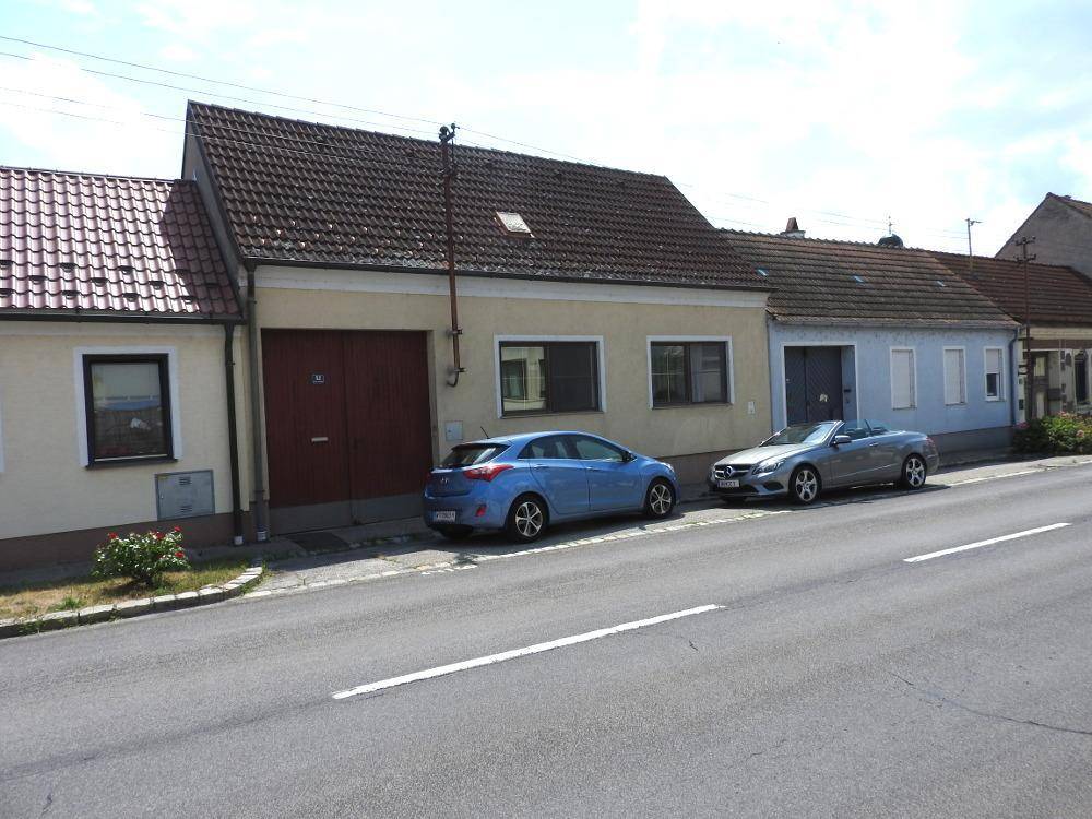 Ansicht des Hauses von der Straße mit zwei geparkten Fahrzeugen und einem traditionellen Satteldach.