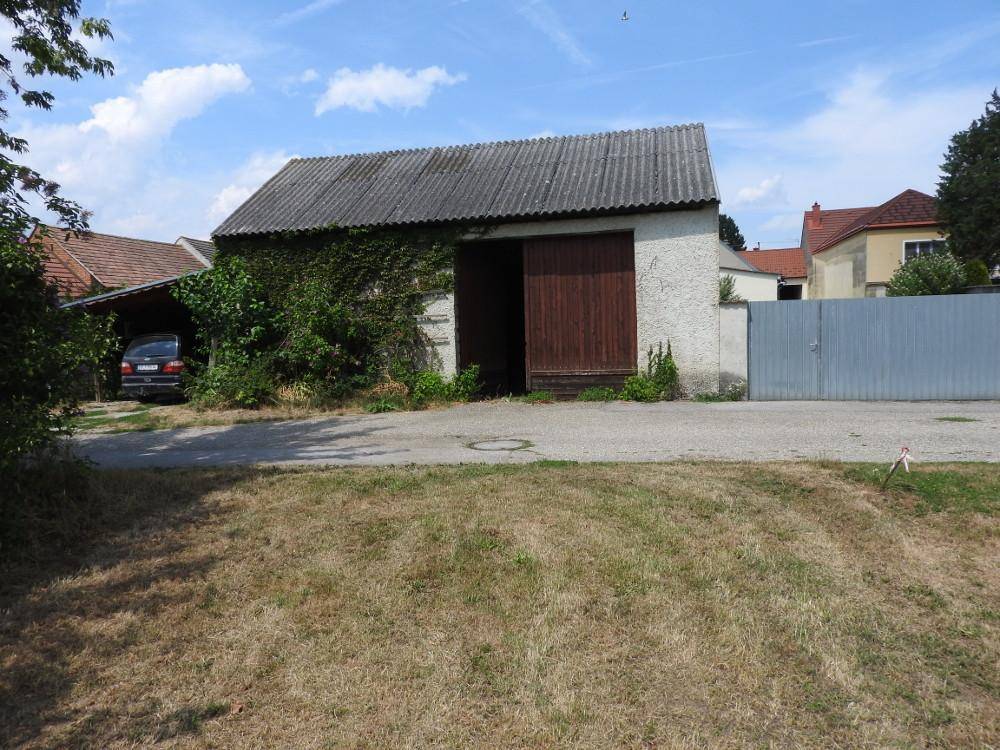Außenansicht einer großen Scheune mit Holztoren und einem Wellblechdach, umgeben von Gras.