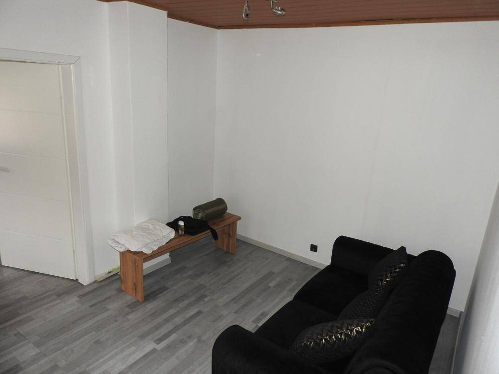 Wohnzimmer mit schwarzem Sofa und einer Holzdecke, die eine gemütliche Atmosphäre schafft.