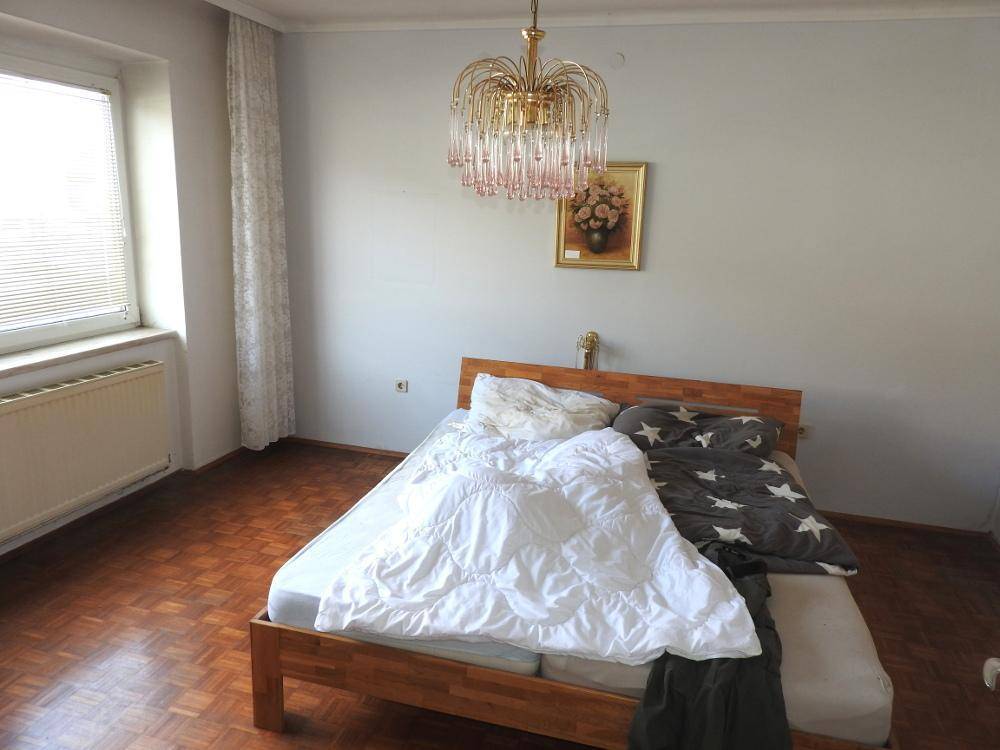 Schlafzimmer mit Parkettboden, einem Doppelbett und einem Kronleuchter, hell durch großes Fenster.
