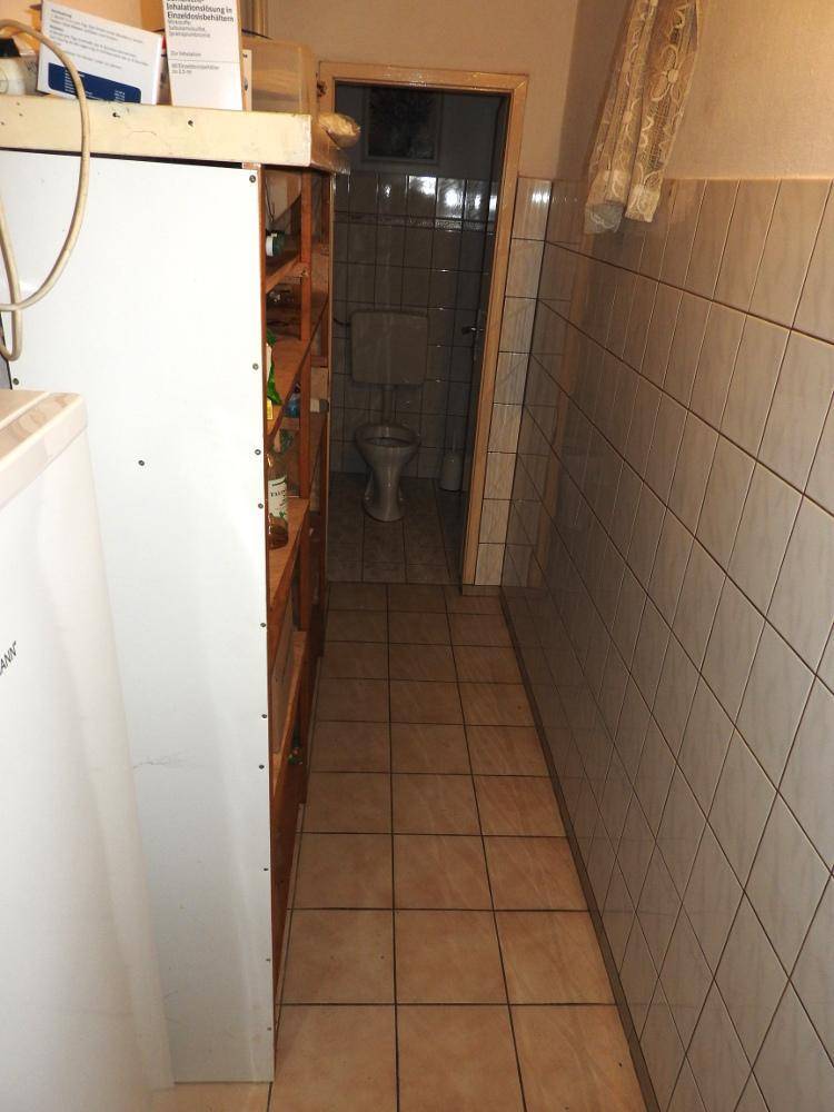 Gefliester Flur, der zu einem separaten WC führt, mit einfachen Wand- und Bodenfliesen.
