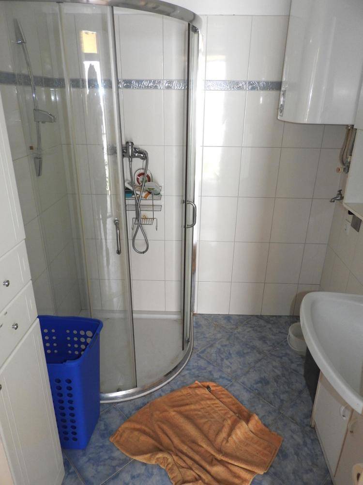 Badezimmer mit Duschkabine, Waschbecken und blauen Bodenfliesen, in einfachem Zustand.