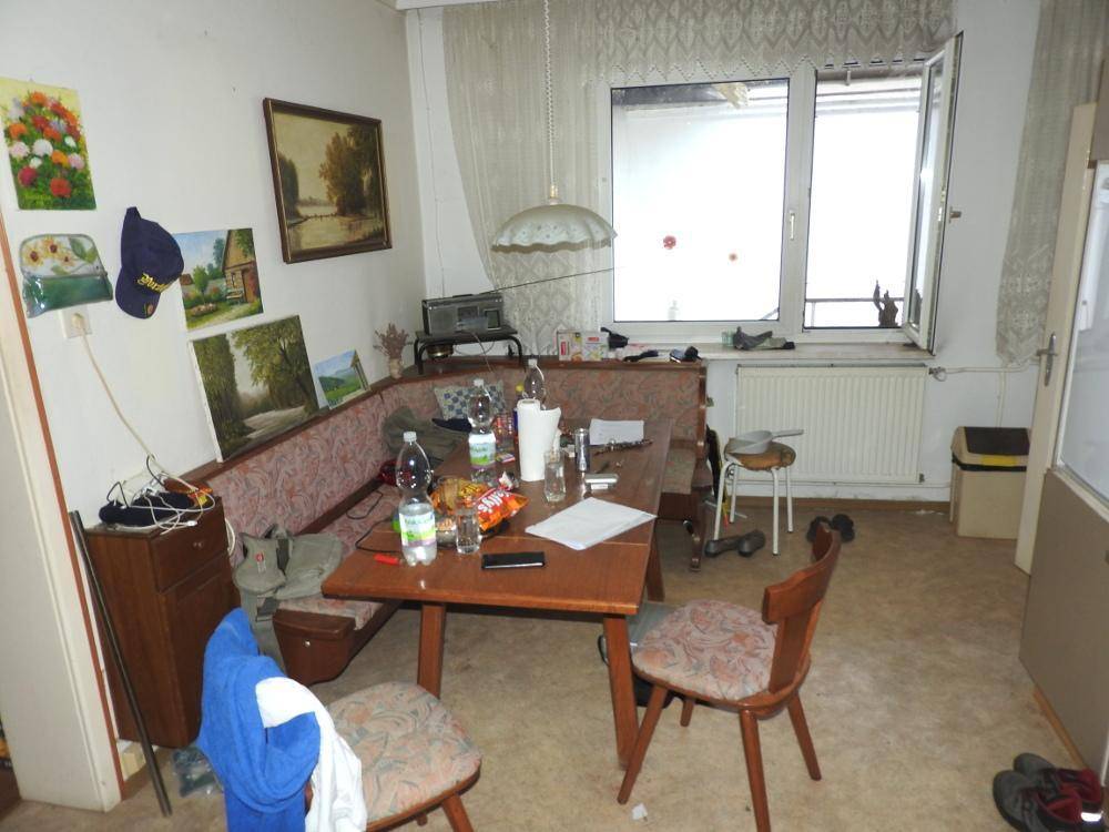 Essbereich mit Eckbank und Holztisch, hell durch ein großes Fenster, mit Renovierungsbedarf.