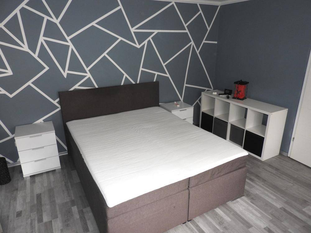 Schlafzimmer mit Doppelbett und einer auffälligen geometrischen Wandgestaltung.