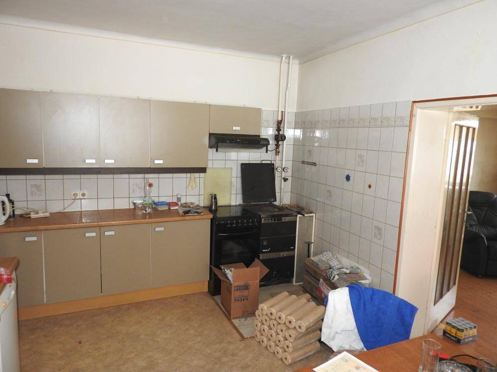 Küche mit beigen Einbauschränken, einem Herd und Fliesen an der Wand, mit Renovierungsbedarf.