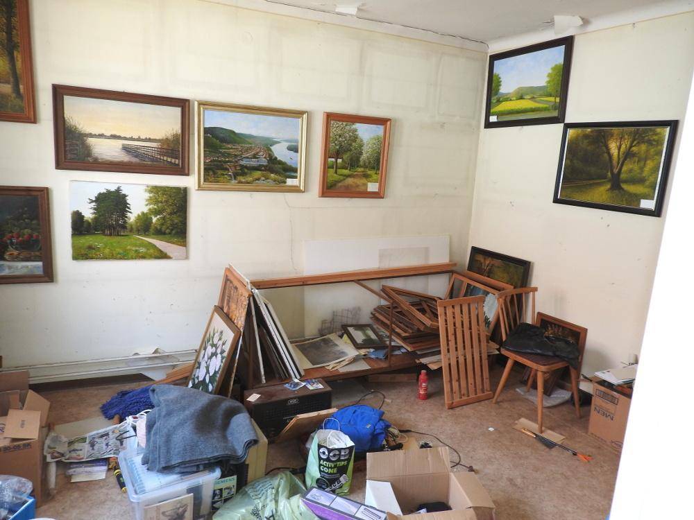 Unaufgeräumter Raum mit vielen Bildern an den Wänden und Renovierungsbedarf, möglicherweise ein Atelier.