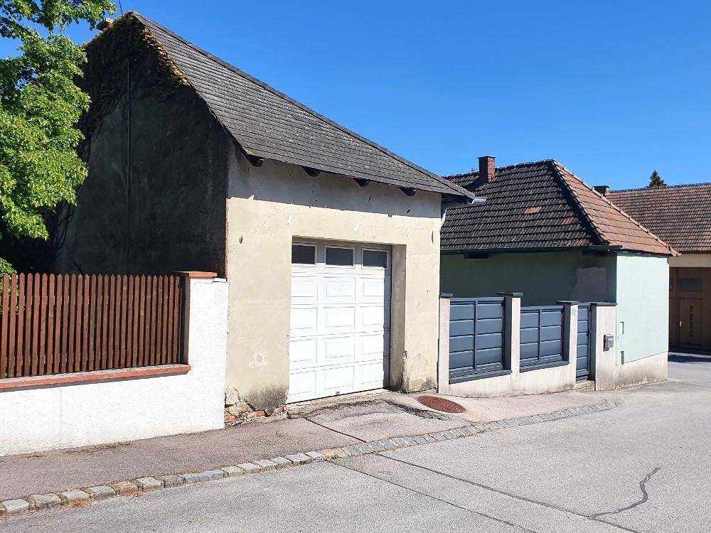 Ansicht der Garage mit Schwingtor und angrenzendem Zaun, umgeben von Grünflächen.