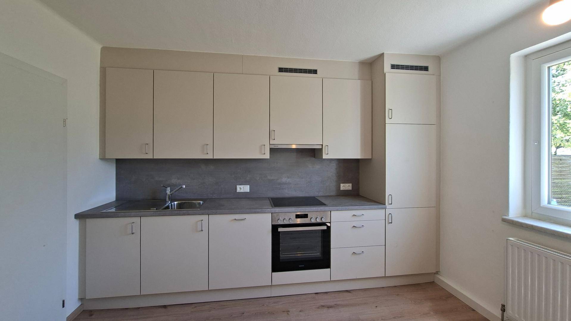 Moderne Einbauküche in Beige mit integrierten Geräten und Arbeitsplatte aus Stein.
