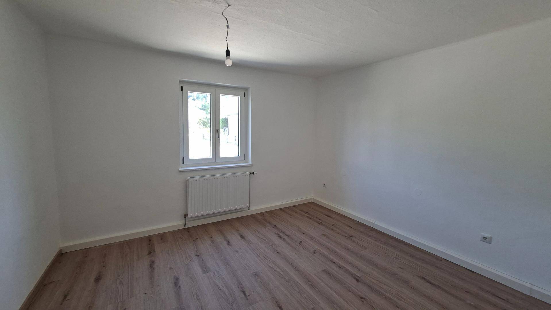 Geräumiges Schlafzimmer mit Laminatboden, weißen Wänden und einem großen Fenster.