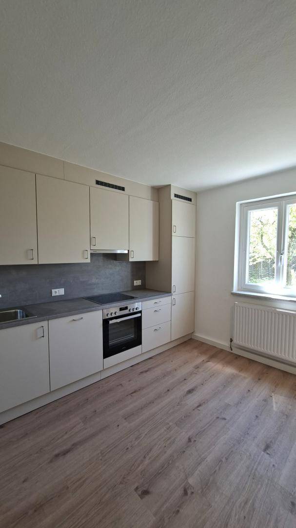 Helle Küche mit beiger Einbauküche, Laminatboden und Fenster mit Blick ins Grüne.
