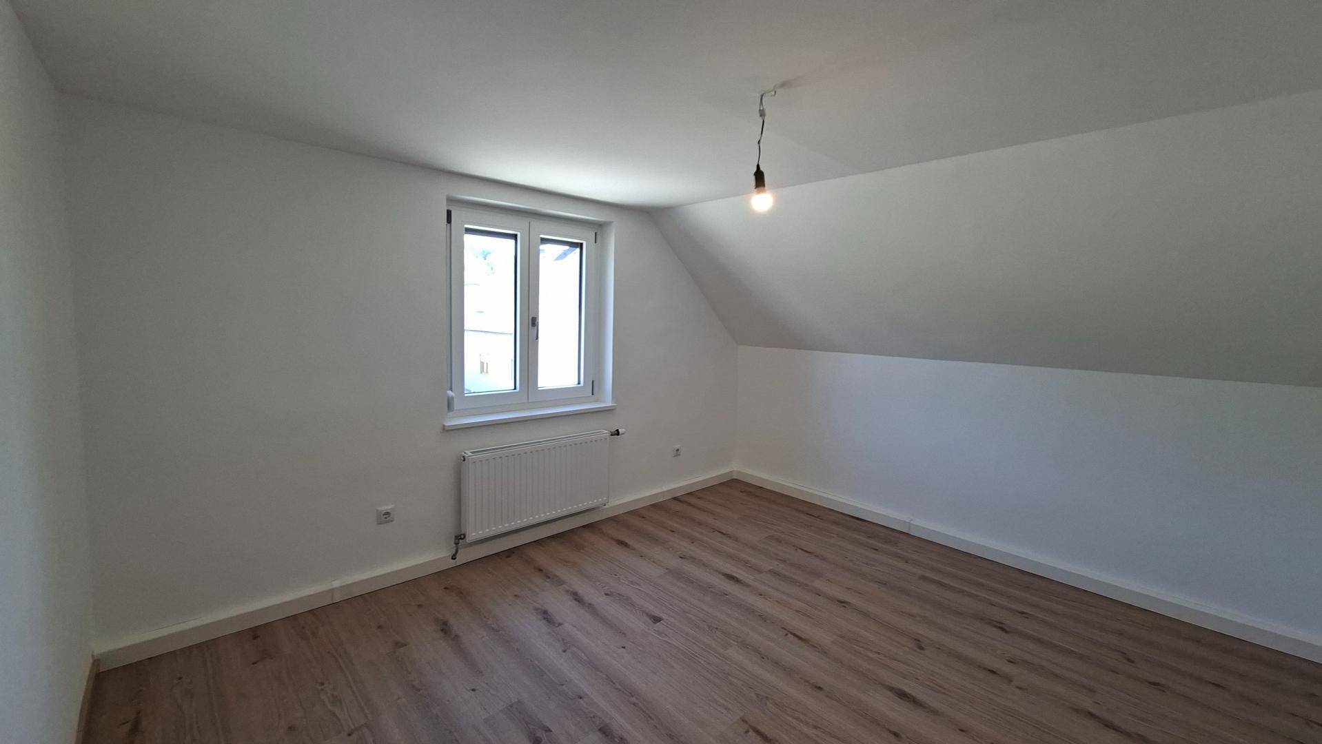 Dachgeschoss-Schlafzimmer mit Laminatboden, weißen Wänden und Fenster.