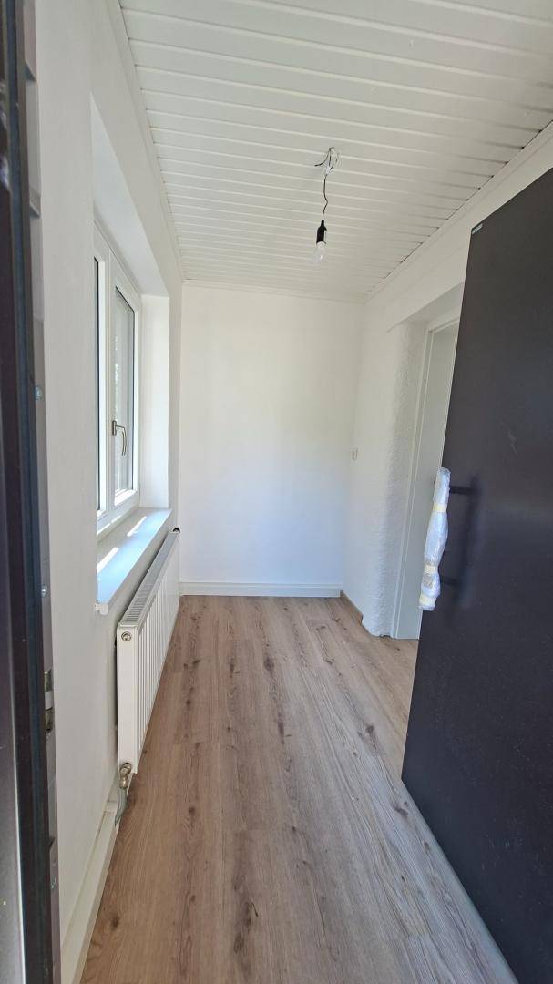 Heller Eingangsbereich mit Laminatboden, weißer Holzdecke und Fenster.