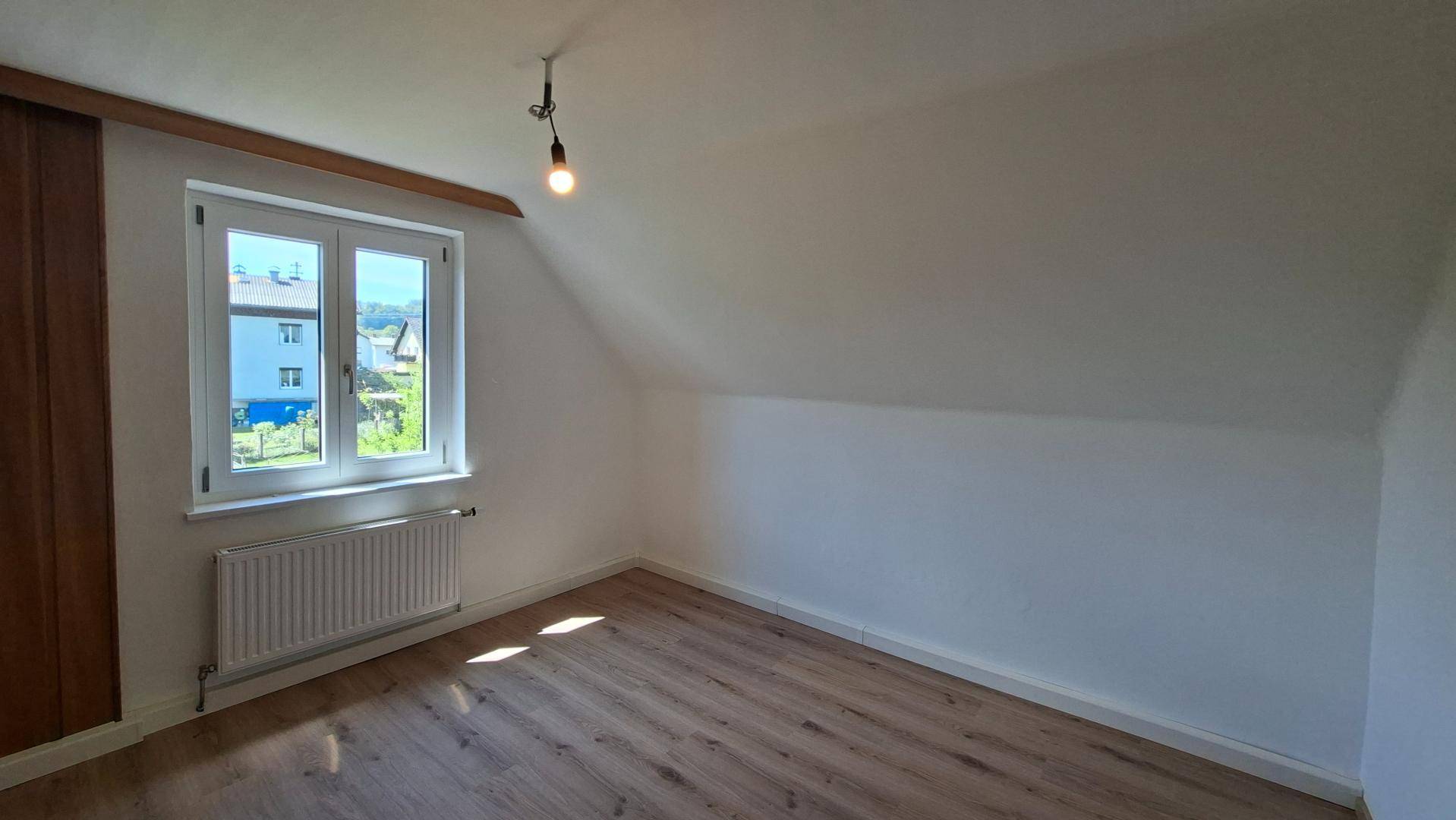 Geräumiges Schlafzimmer im Dachgeschoss mit Laminatboden und Blick auf die Nachbarschaft.