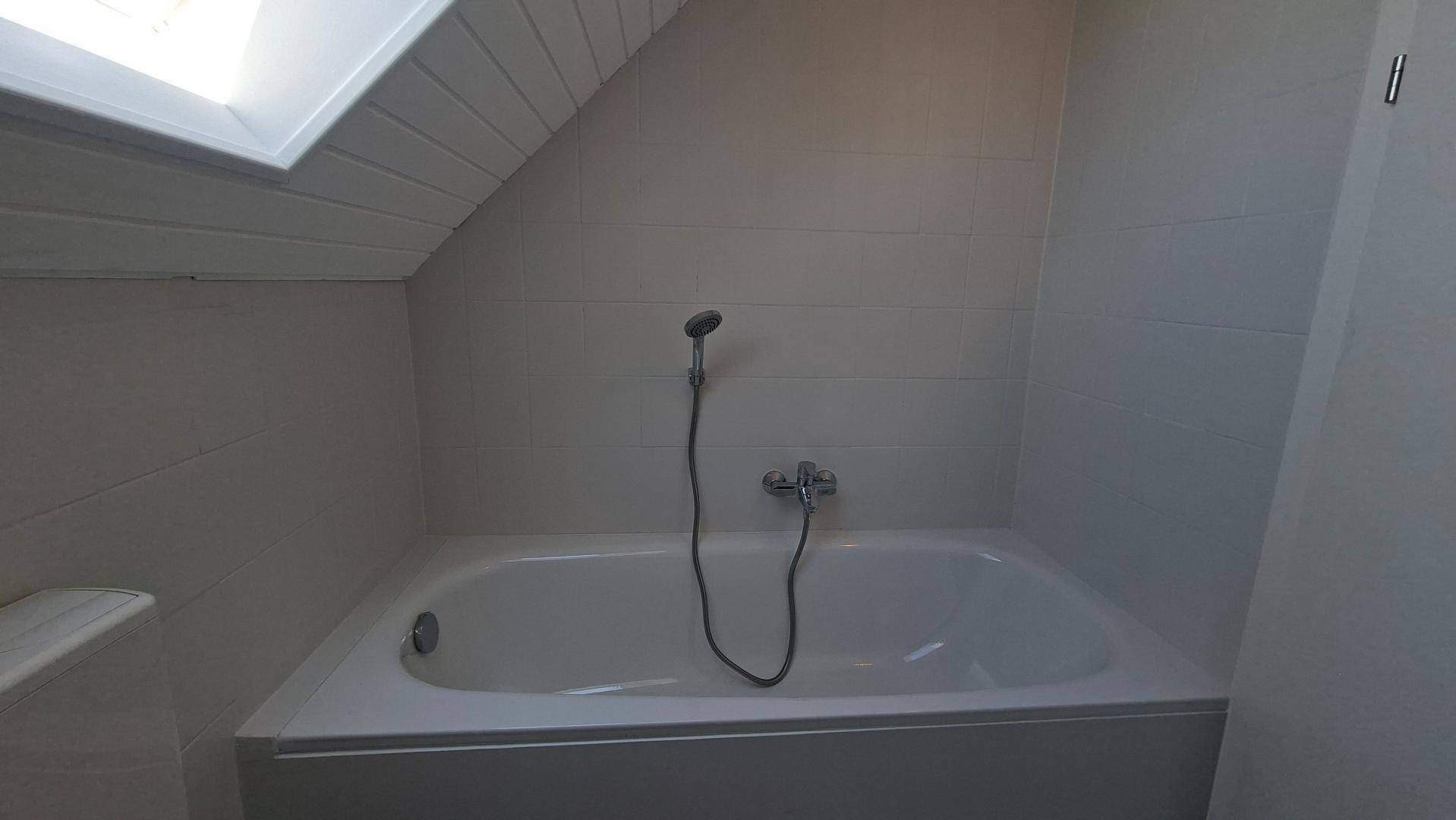 Eingebaute Badewanne im Dachgeschoss-Badezimmer mit weißen Fliesen und Dachschräge.