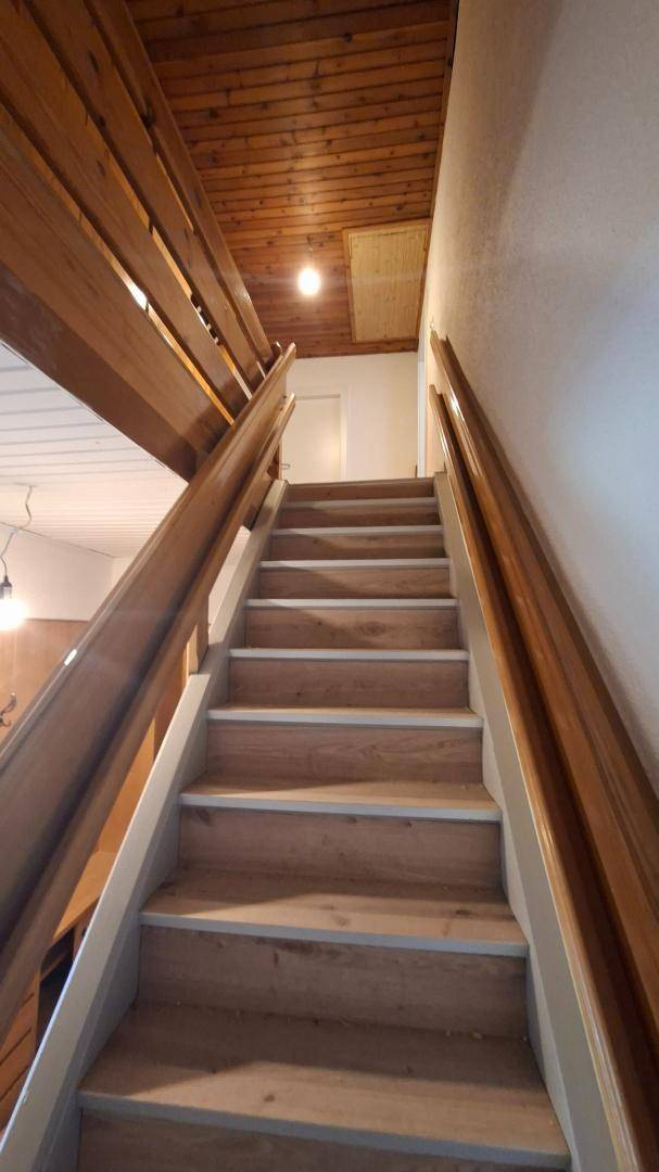 Holztreppe führt zum oberen Stockwerk mit Holzvertäfelung und natürlichem Lichteinfall.