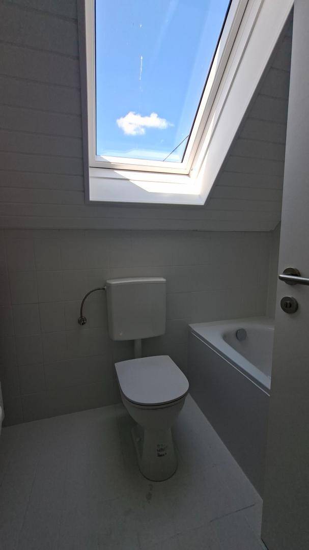 Modernes Badezimmer im Dachgeschoss mit Toilette, Badewanne und Dachfenster.