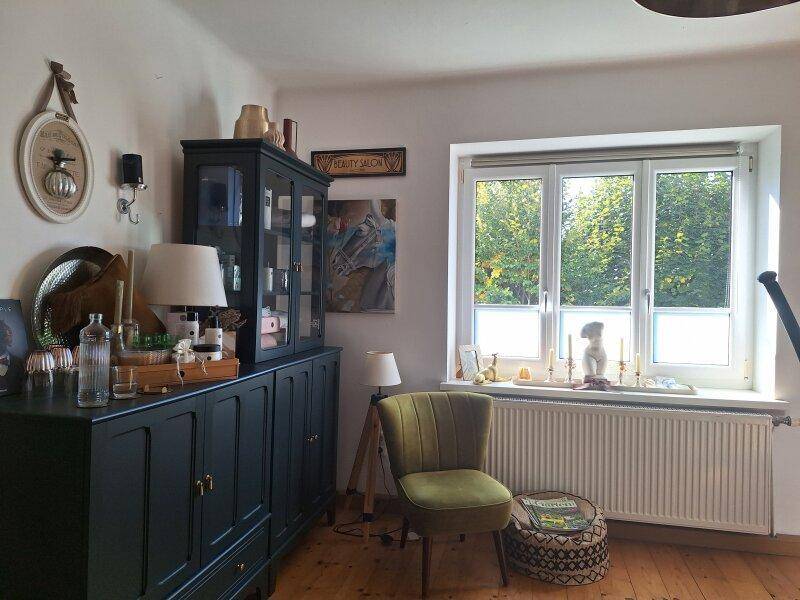 Heller Raum mit Holzboden, großem Fenster und einem grünen Sessel, ideal zum Entspannen.