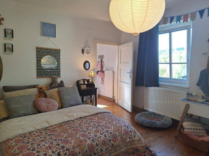 Gemütliches Schlafzimmer mit Holzboden, großem Fenster und dekorativen Kissen.