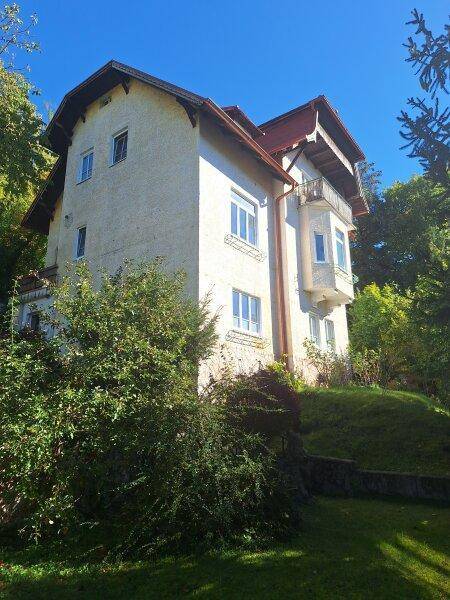 Charmantes Haus mit heller Fassade und traditionellem Dach, eingebettet in grüne Natur.