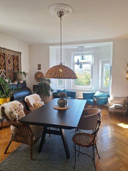 Eleganter Essbereich mit Holztisch, Korbstühlen und großen Fenstern mit Blick ins Grüne.