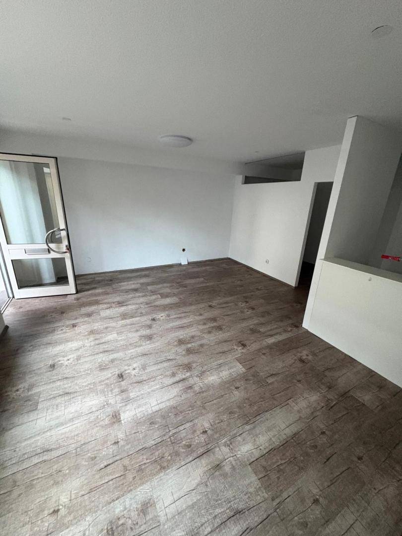 Leerer Raum mit hellem Laminatboden in Holzoptik und weißen Wänden, eine Glastür ist sichtbar.