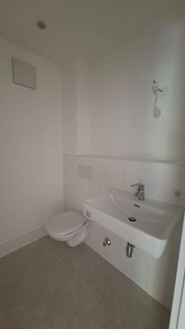 Helles Gäste-WC mit wandhängender Toilette, modernem Waschbecken und grauen Bodenfliesen.