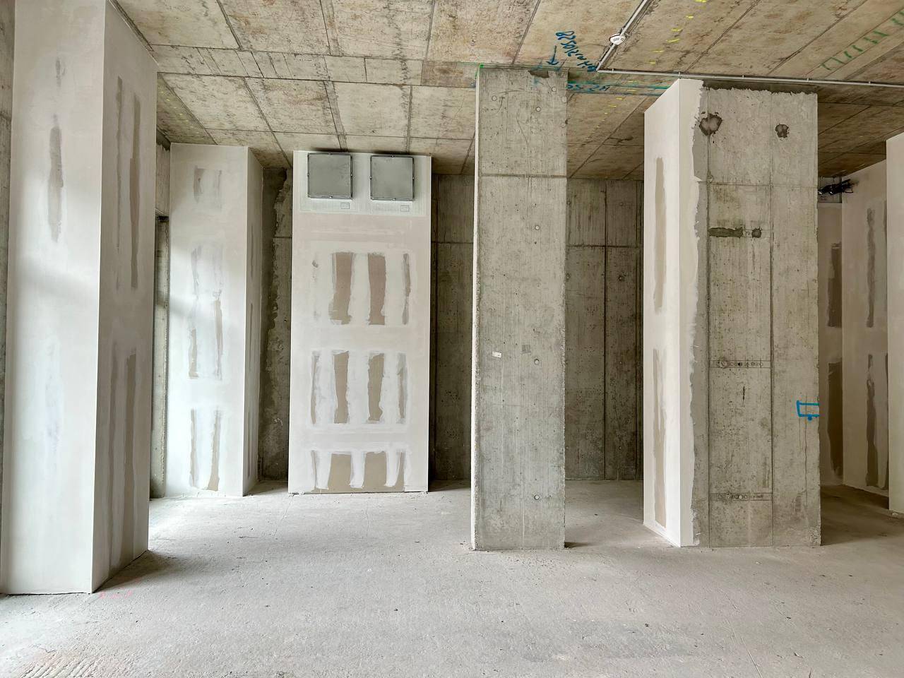Großer Rohbau-Innenraum mit Betonstützen und teilweise verputzten Trockenbauwänden.