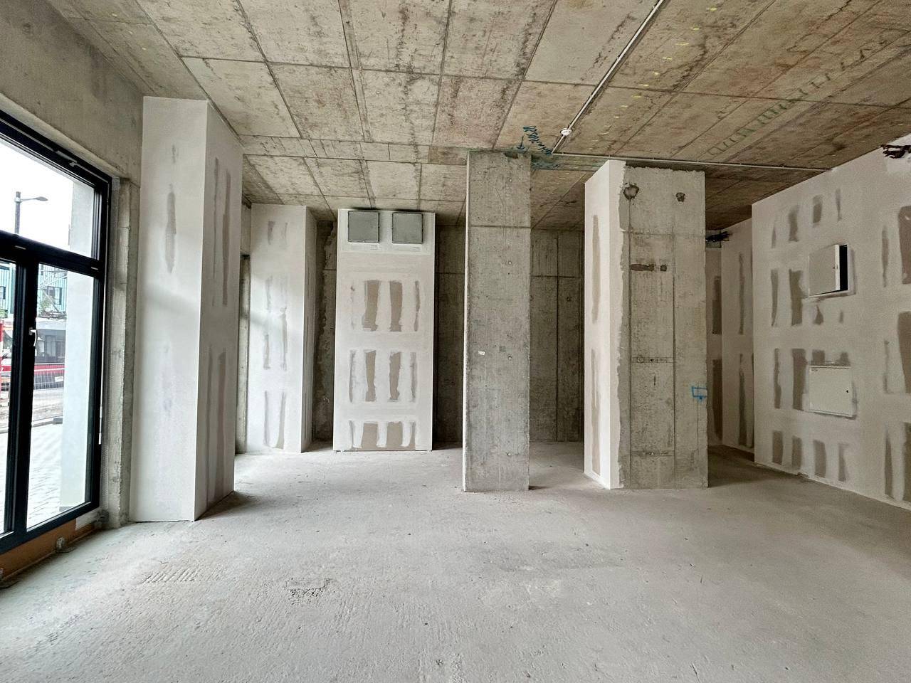 Rohbau-Innenraum mit Betonstützen, vorbereiteten Wänden und großen Fensterbereichen.