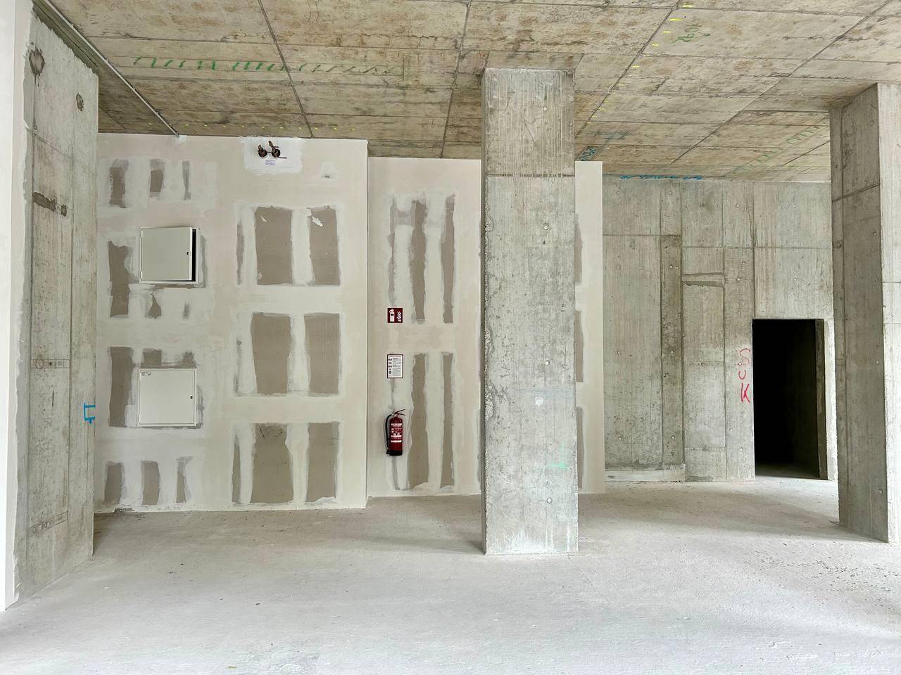 Rohbau-Innenraum mit Betonstützen, vorbereiteten Wänden und einem Feuerlöscher an der Wand.
