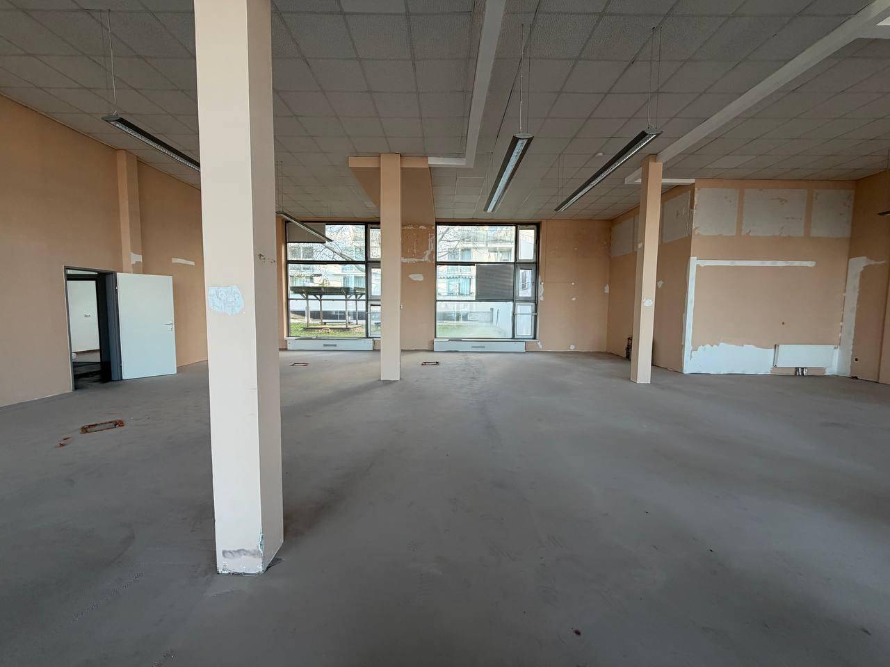 Weitläufiger Gewerberaum mit vielen Fenstern, Säulen und einem Eingangsbereich, bereit für den Ausbau.