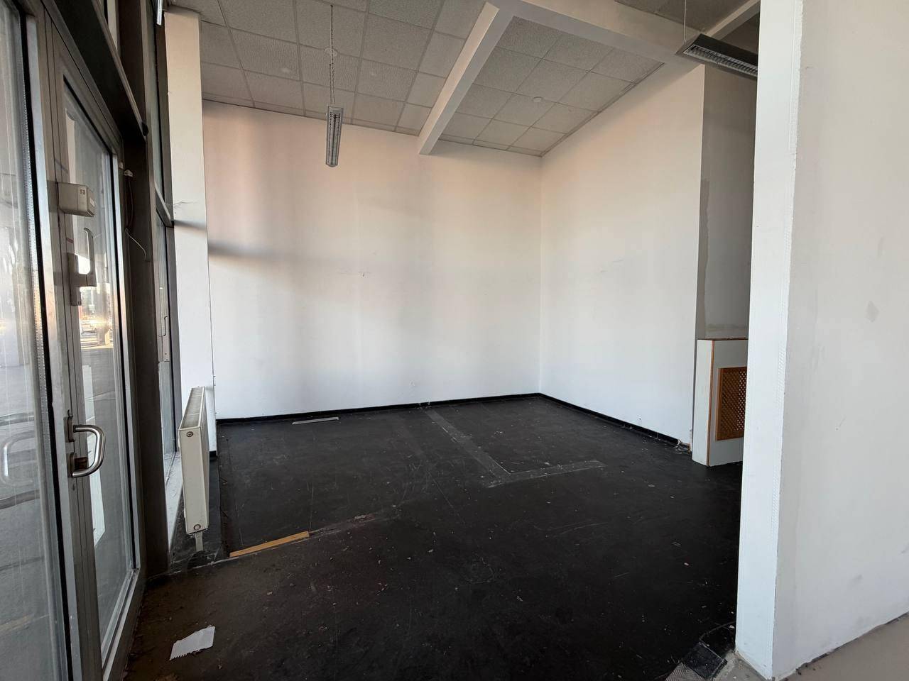 Kleinerer Gewerberaum mit dunklem Boden, weißen Wänden und einem Fenster zur Straße.