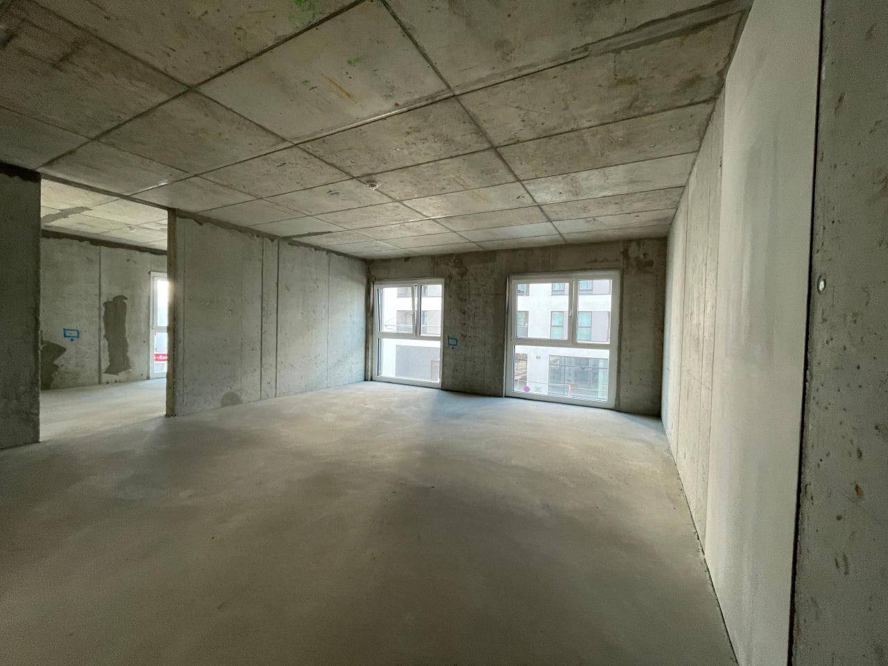 Geräumiger Rohbau mit Betonoberflächen und großen Fenstern, die einen Blick auf die Umgebung bieten.