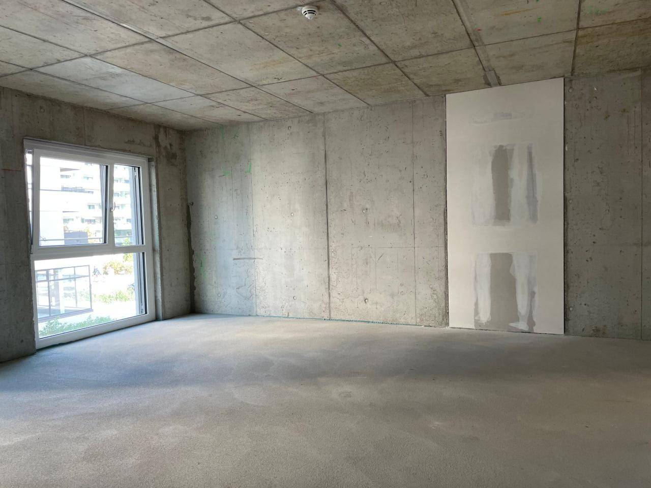 Rohbauzimmer mit einer großen Fensterfront und einer teilweise verputzten Wand, bereit für den Ausbau.