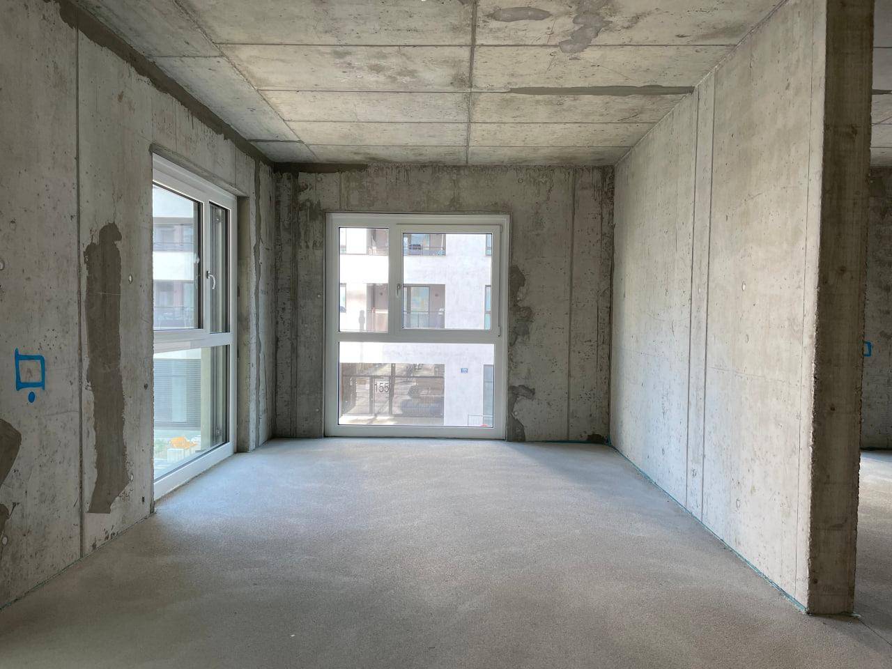 Rohbauzimmer mit Betonwänden und einem großen Fenster, das viel natürliches Licht hereinlässt.