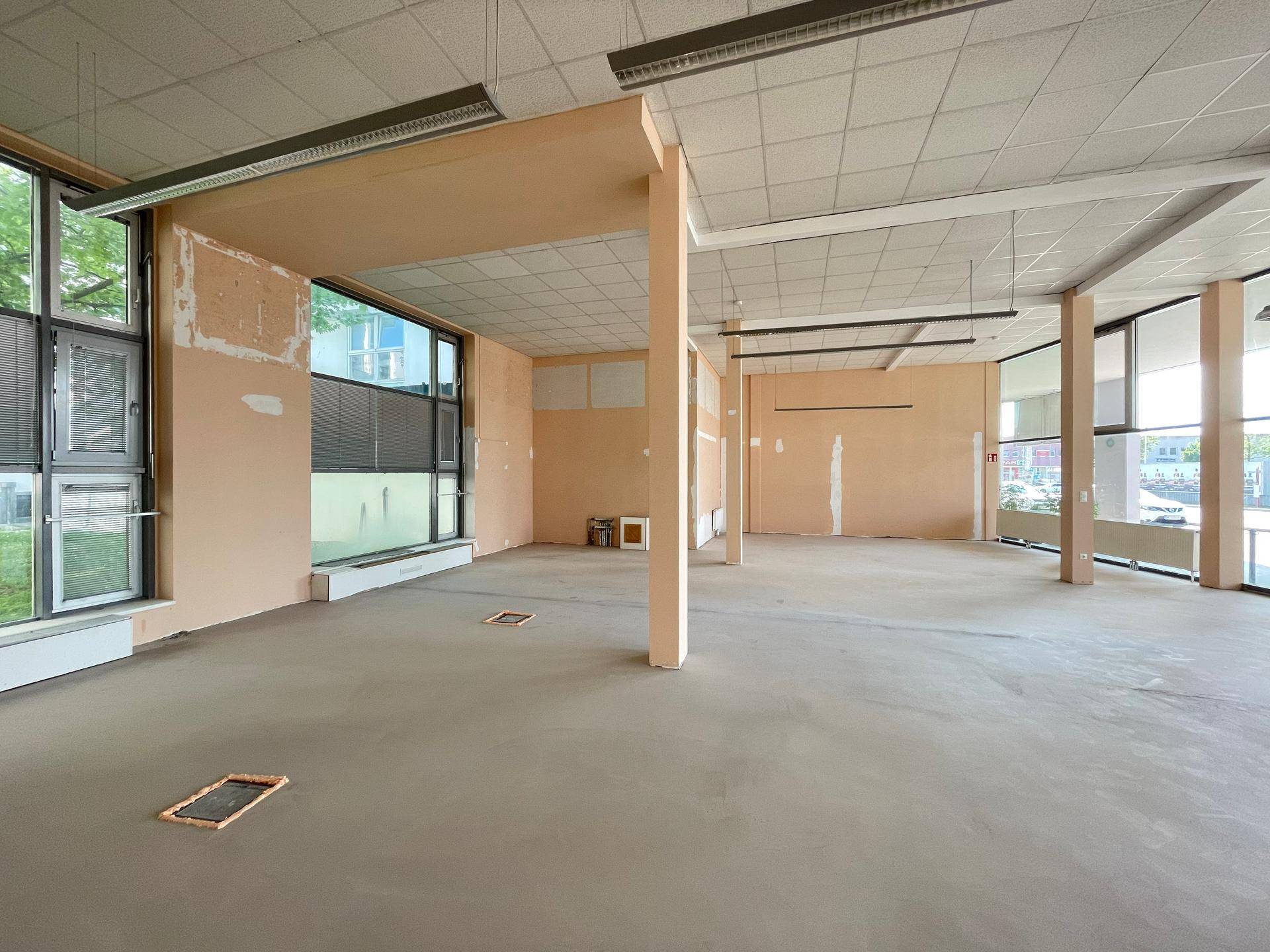 Großer, leerer Gewerberaum mit hohen Decken, großen Fenstern und sichtbaren tragenden Säulen.