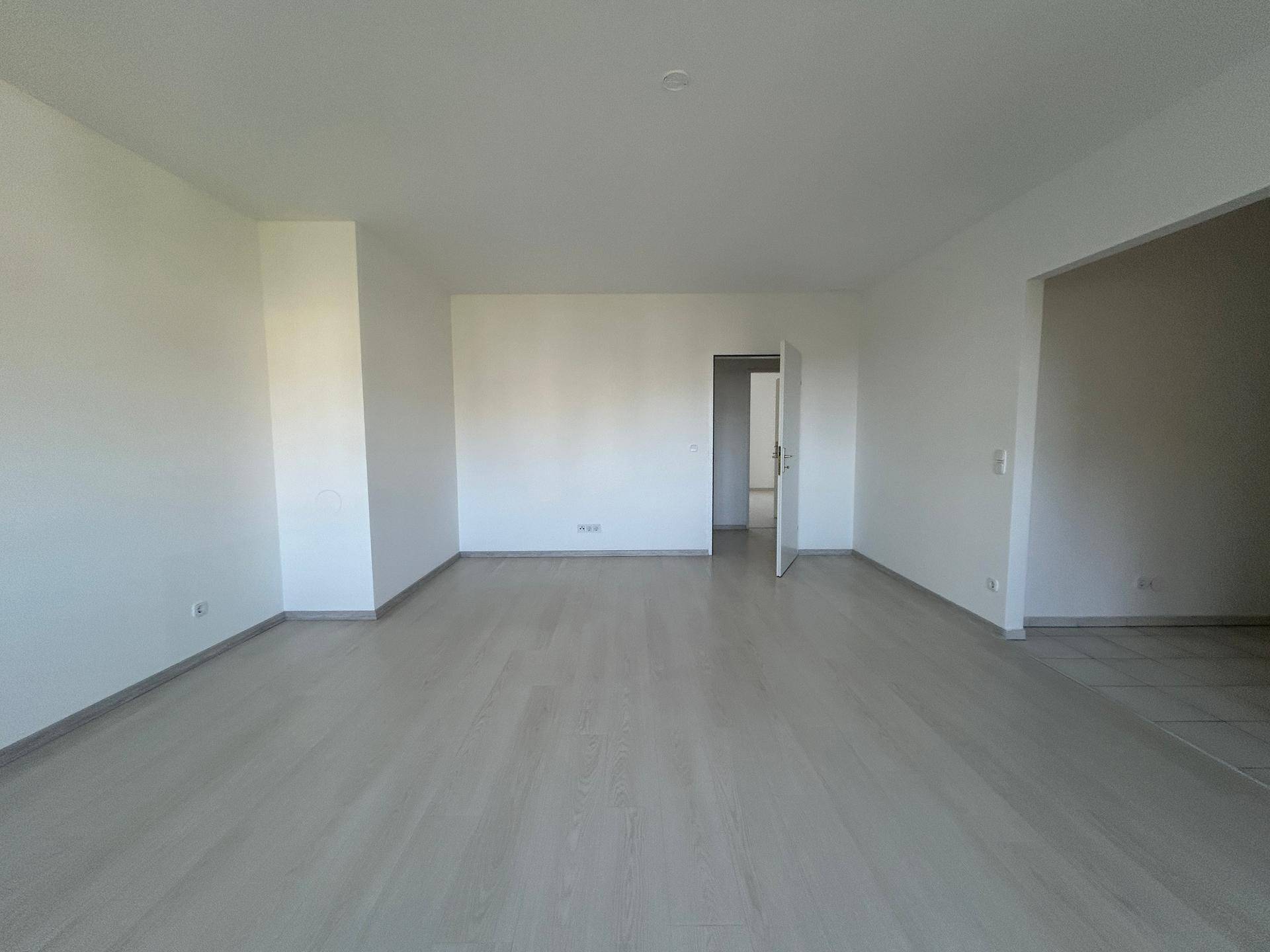 Weitläufiges Wohnzimmer mit hellem Laminatboden und Zugang zu anderen Räumen.