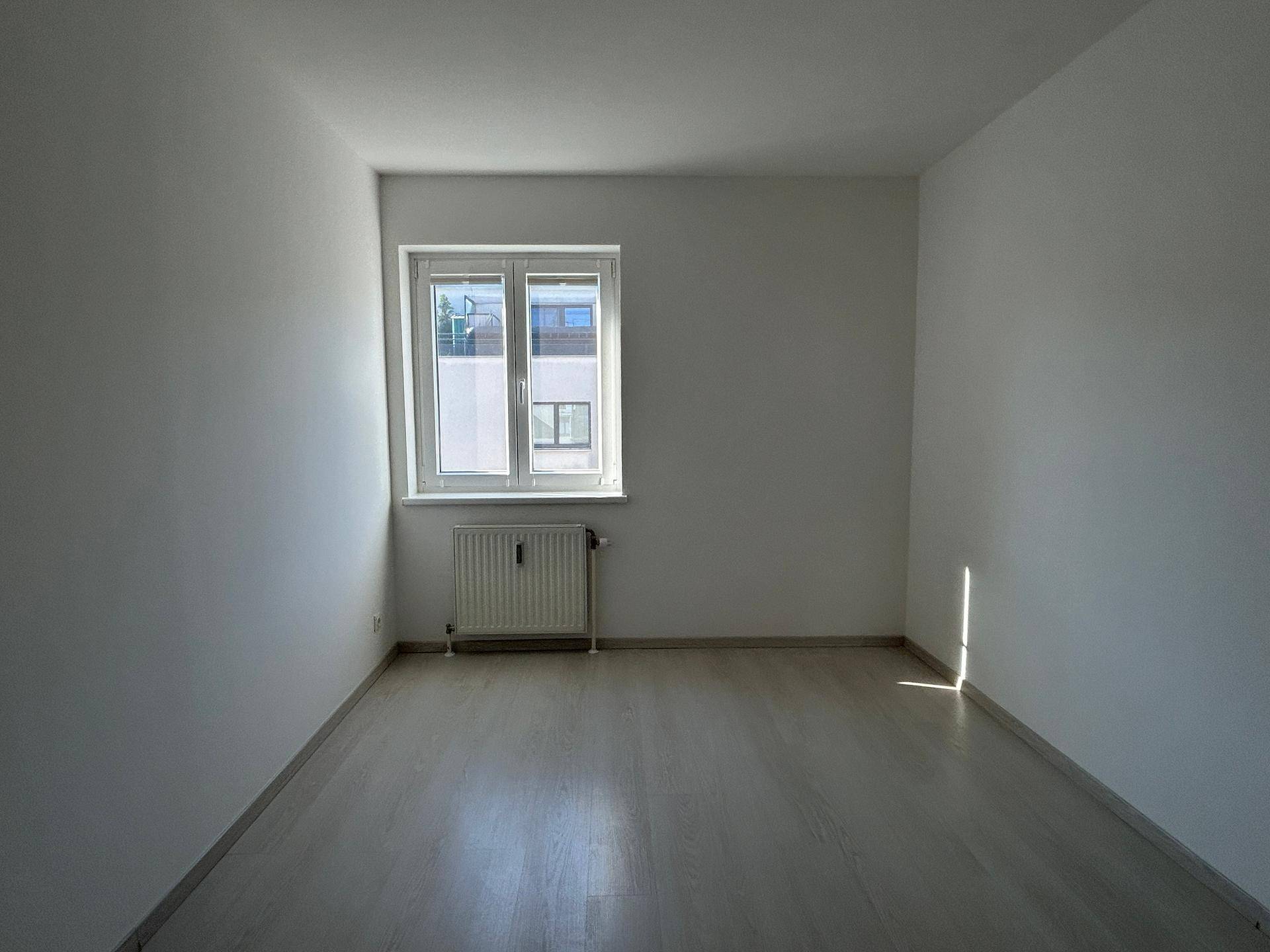 Geräumiges Schlafzimmer mit hellem Laminatboden und einem Fenster, das den Raum erhellt.