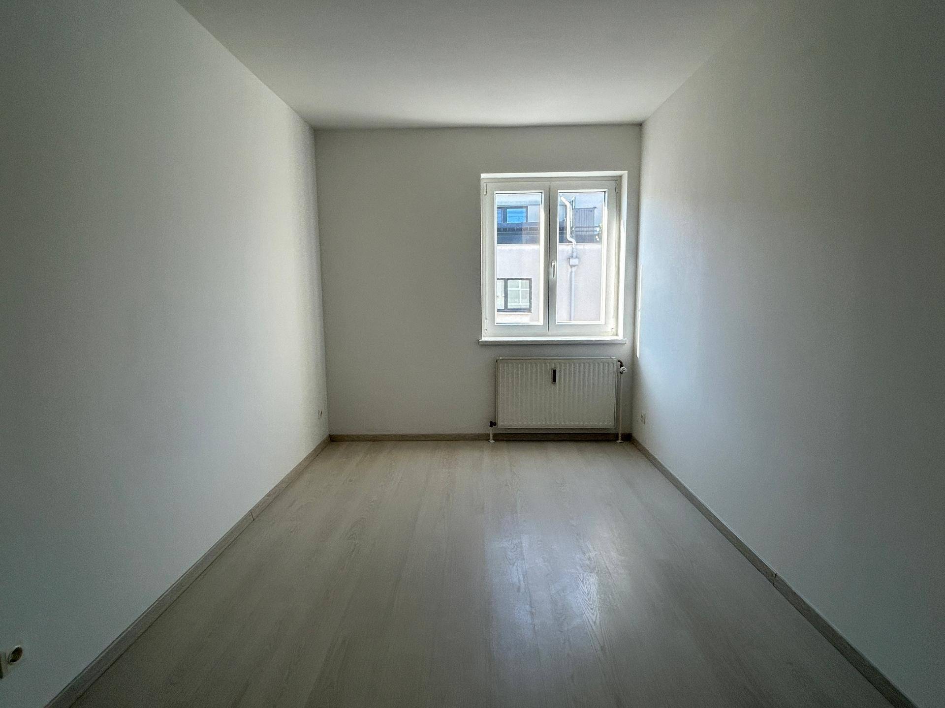 Helles Schlafzimmer mit Laminatboden und einem Fenster, das viel natürliches Licht hereinlässt.
