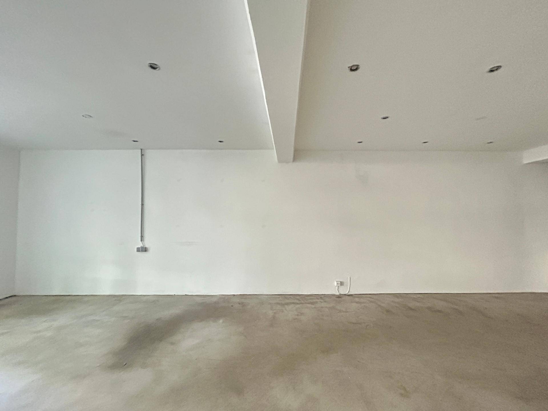 Weitläufiger Gewerberaum mit weiß gestrichenen Wänden und einem schlichten Betonboden, ideal für verschiedene Nutzungen.