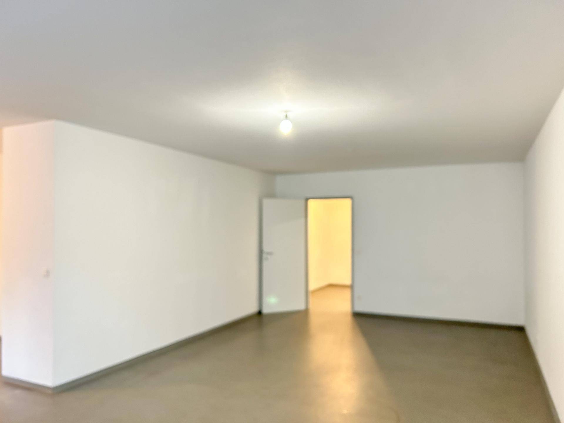 Geräumiger, leerer Wohnbereich mit weiß gestrichenen Wänden und einer offenen Tür zu einem Nebenraum.